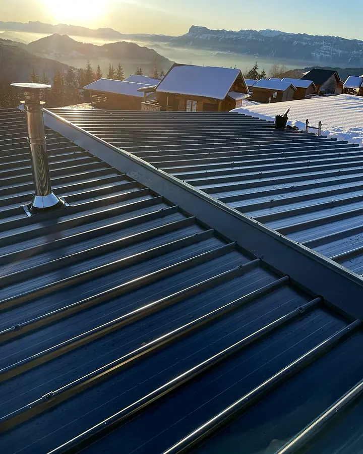 Couverture en bac acier anthracite terminée sur un chalet en montagne, au lever du soleil, face à une mer de nuages. Chantier de Trois Massifs Toiture.
